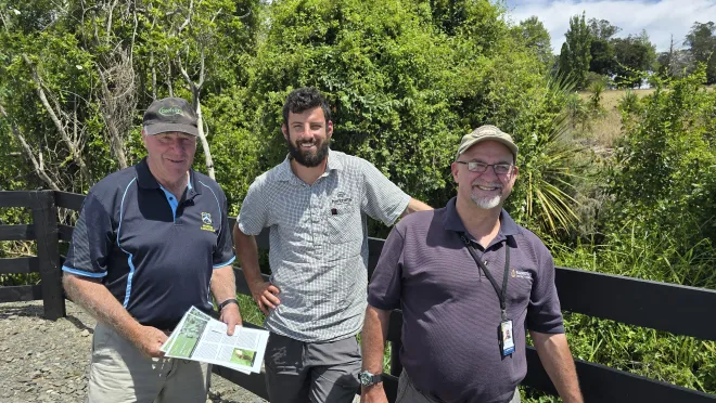 Three men standing in front of a black fence at the entrance to Tutaenui Reservoir. From left to right they are David Smith, Rory Johnson and Neil Gallagher.